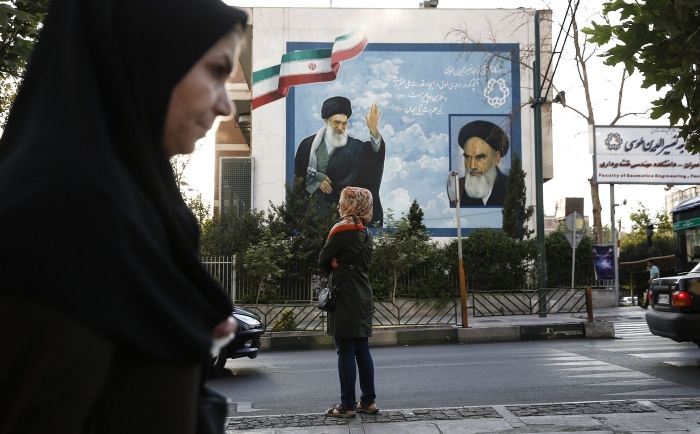 Pedestrians pass a wall mural depicting Ayatollah Ali Khamenei